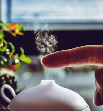 A hand touches mist rising from a diffuser, creating a relaxing ambiance indoors.