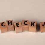 Wooden blocks aligned to spell 'CHECK' with a checkmark symbol on a neutral background.